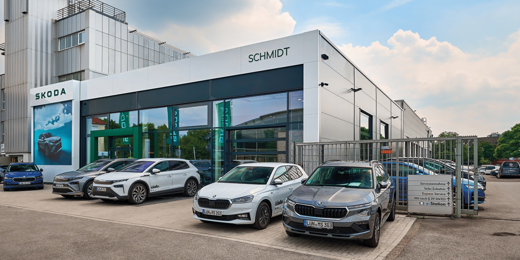 ußenansicht des ŠKODA Autohauses Schmidt in Lünen mit mehreren geparkten ŠKODA Fahrzeugen vor dem Gebäude und sichtbarem Eingang zum Haus.