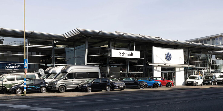 Der Haupteingang des Volkswagen-Gebäude der Autowelt Schmidt am Standort Lünen. Über dem Eingang das VW Logo, daneben ein großes Schild mit der Aufschrift "Schmidt". Vor dem Glasgebäude stehen viele VW Modelle.